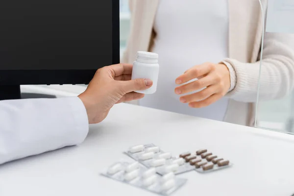 Visão cortada de farmacêutico dando garrafa com vitaminas para a mulher grávida no balcão — Fotografia de Stock