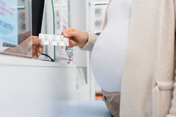 Vista recortada del farmacéutico que administra blíster con medicamento a la mujer embarazada en el mostrador - foto de stock