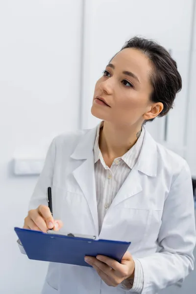 Tattooed pharmacist in white coat writing on clipboard — Stock Photo