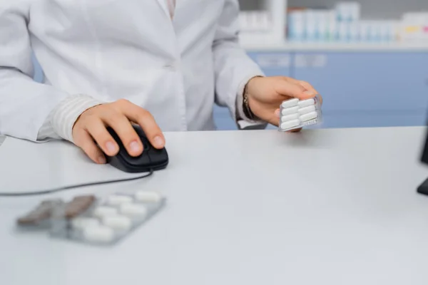 Обрізаний вид фармацевта, який тримає блістерний пакет і використовує комп'ютерну мишу в аптеці — стокове фото
