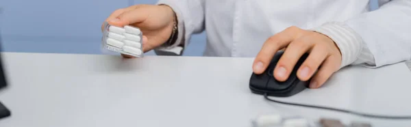 Vista recortada del envase del blíster de la celebración del farmacéutico y el uso del ratón de la computadora en la farmacia, bandera - foto de stock