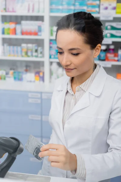 Farmacéutico tatuado sosteniendo blíster cerca del escáner en la farmacia - foto de stock