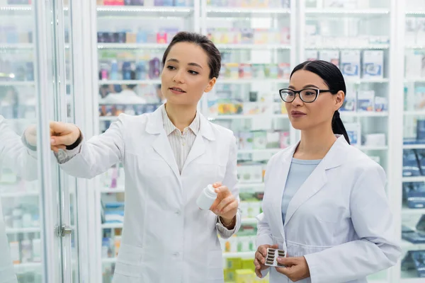 Farmacêuticos inter-raciais em casacos brancos segurando medicação na farmácia — Fotografia de Stock