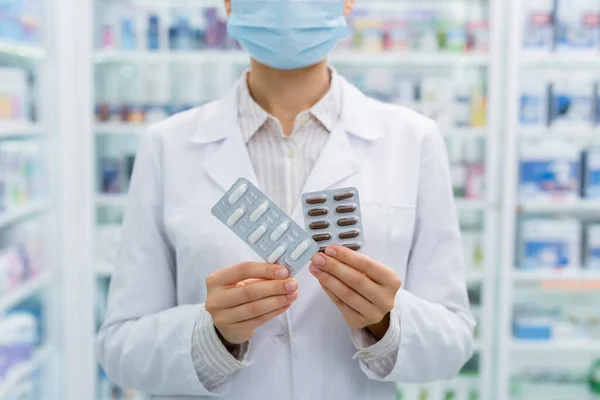 Cropped view of apothecary in medical mask holding blister packs with medication — Stock Photo