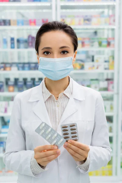 Boticário em máscara médica segurando blisters com medicação — Fotografia de Stock