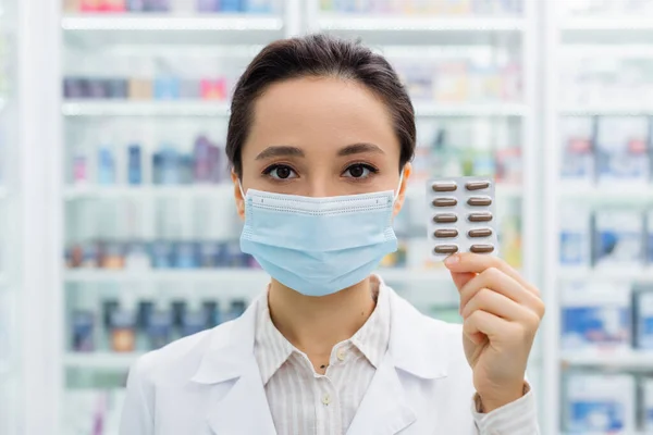 Аптекарь в медицинской маске держит пузырь пакет с лекарствами — стоковое фото