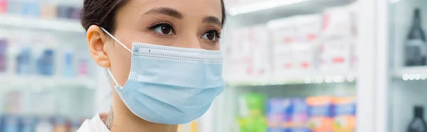 Tatuado boticário em máscara médica olhando para longe na farmácia, banner — Fotografia de Stock