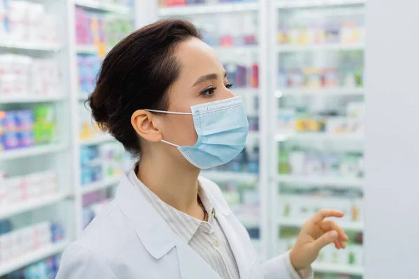 Tattooed apothecary in medical mask looking away in drugstore — Stock Photo