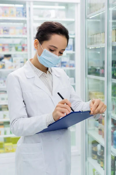 Аптекаря в медичній масці, що пише на кишені — стокове фото