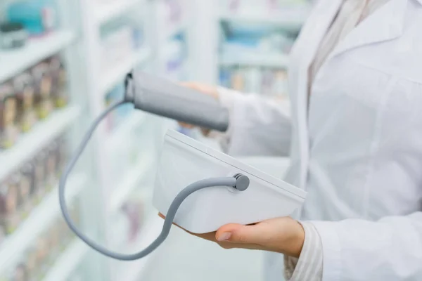 Vista recortada de farmacéutico en blanco abrigo celebración tonómetro digital en farmacia - foto de stock