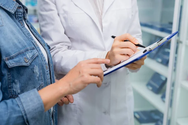 Vue recadrée du client pointant vers le presse-papiers près du pharmacien — Photo de stock