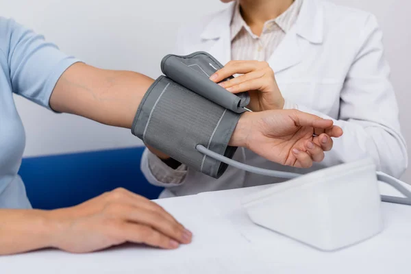 Vista ritagliata del medico in tonometro di regolazione cappotto bianco sulla donna — Foto stock