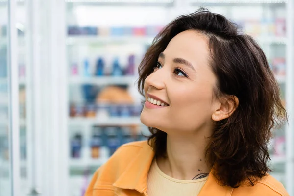 Tattooed woman looking away and smiling in drugstore — Stock Photo