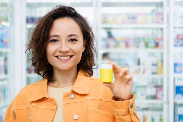 Татуйована жінка посміхається, тримаючи пляшку з таблетками в аптеці — стокове фото