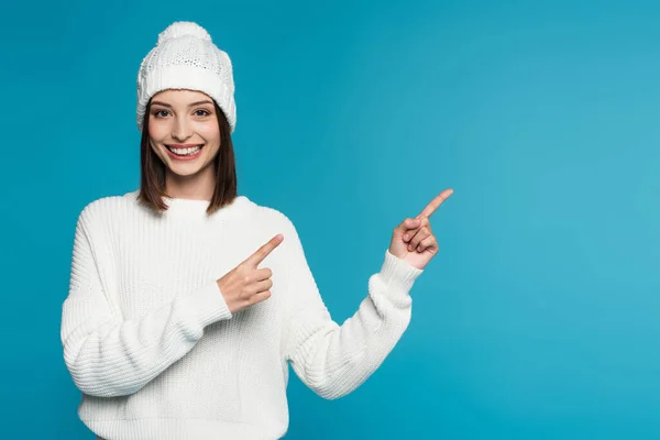 Donna sorridente in caldo cappello e maglione che punta con le dita isolate sul blu — Foto stock