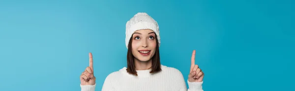 Bruna donna in maglia cappello punta con le dita isolate su blu, striscione — Foto stock