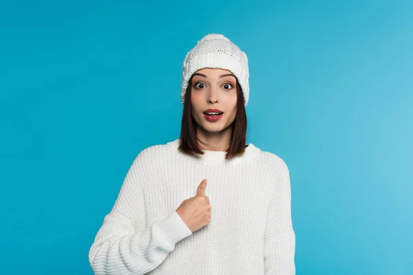 Amazed woman in warm clothes pointing with finger isolated on blue — Stock Photo