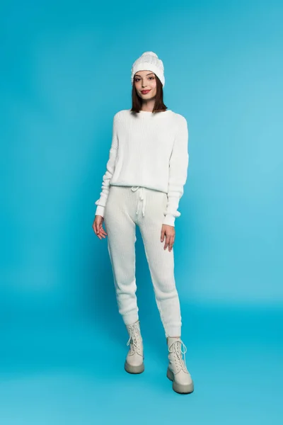 Pleine longueur de femme souriante en tricot regardant la caméra sur fond bleu — Photo de stock