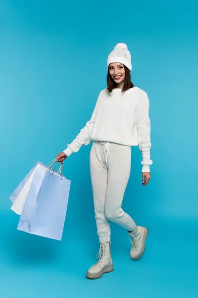 Mujer positiva con bolsas de compras caminando sobre fondo azul - foto de stock