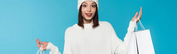 Mulher excitada em roupas quentes segurando sacos de compras isolados em azul, banner — Fotografia de Stock