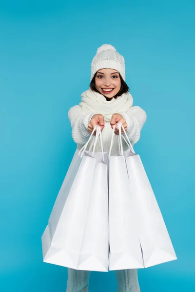 Femme gaie en vêtements chauds montrant des sacs à provisions à la caméra isolée sur bleu — Photo de stock