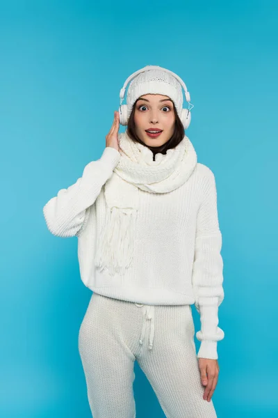 Amazed woman in knitted clothes listening music in headphones isolated on blue — Stock Photo