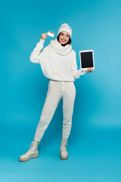 Full length of woman in knitted clothes holding digital tablet with blank screen and credit card on blue background — Stock Photo