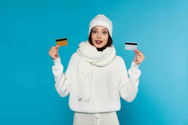 Astonished woman in knitted clothes holding credit cards isolated on blue — Stock Photo