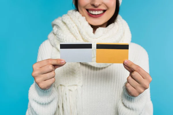 Cropped view of blurred woman in knitted sweater holding credit cards isolated on blue — Stock Photo