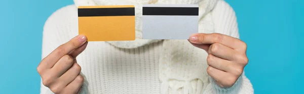 Cropped view of blurred woman in sweater holding credit cards isolated on blue, banner — Stock Photo