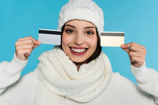 Donna in bianco vestiti caldi sorridente alla fotocamera e in possesso di carte di credito isolate su blu — Foto stock