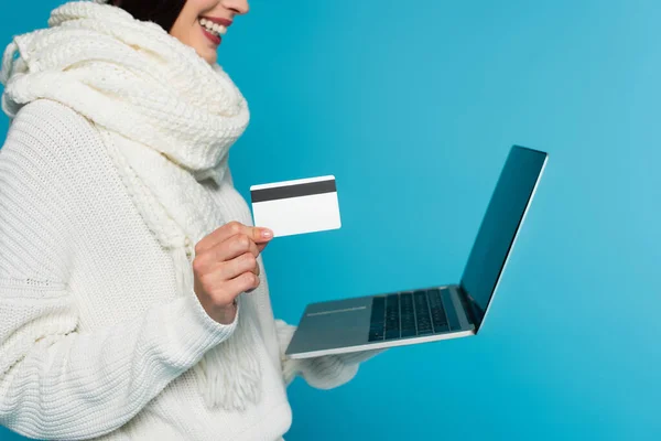 Cropped view of blurred woman in knitted sweater holding laptop and credit card isolated on blue — Stock Photo