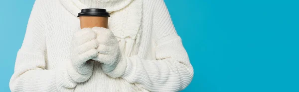 Vue recadrée d'une femme vêtue de vêtements et de gants blancs chauds tenant une tasse en papier isolée sur une bannière bleue — Photo de stock