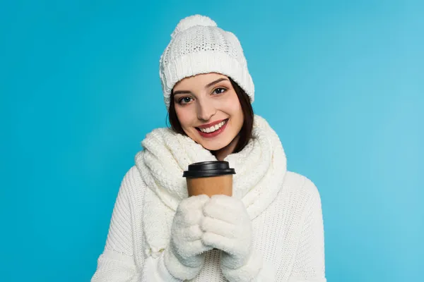 Positive woman in gloves and warm scarf holding paper cup isolated on blue — Stock Photo