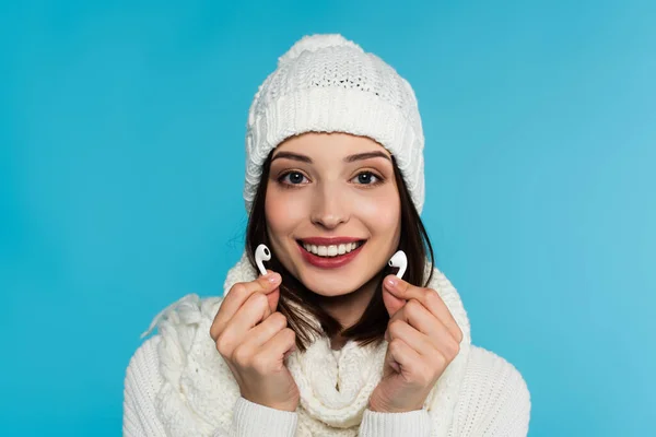 Bella donna in maglia cappello e sciarpa in possesso di auricolari wireless isolati su blu — Foto stock