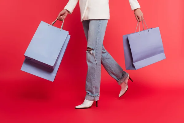 Vista cortada de mulher elegante segurando sacos de compras no fundo vermelho — Fotografia de Stock