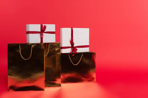 Gifts in golden shopping bags on red background — Stock Photo