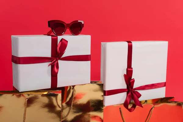 Sunglasses on present near shopping bags isolated on red — Stock Photo
