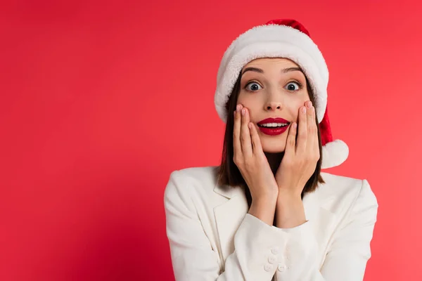 Verblüffte Frau mit roten Lippen und Weihnachtsmannmütze, die isoliert auf rot in die Kamera blickt — Stockfoto
