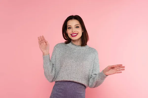 Mulher sorridente em camisola quente acenando para a câmera isolada em rosa — Fotografia de Stock