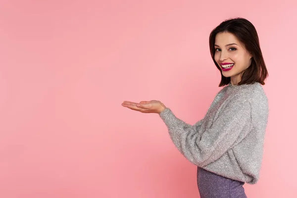 Mujer feliz en suéter cálido apuntando con las manos aisladas en rosa - foto de stock