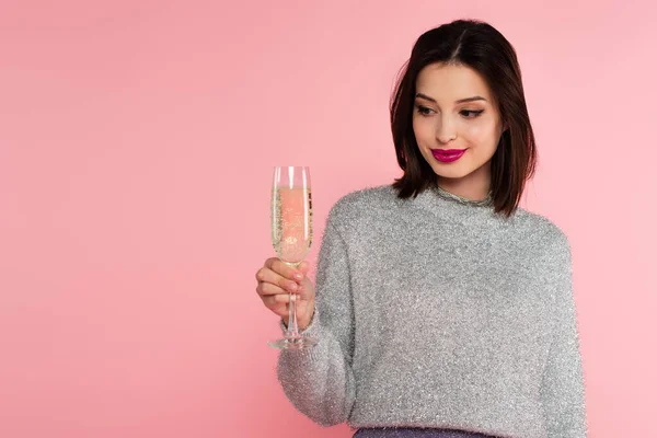 Bruna donna in maglione guardando un bicchiere di champagne isolato su rosa — Foto stock