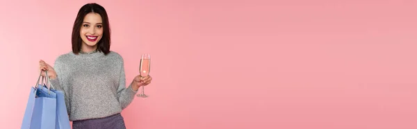 Hübsche Frau im Pullover mit Einkaufstaschen und Champagner auf rosa Banner — Stockfoto