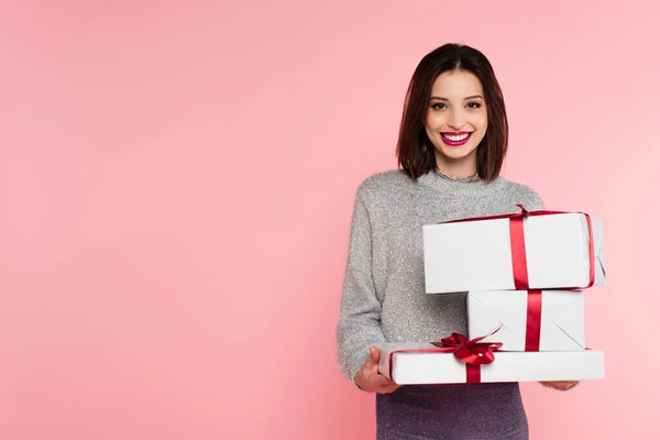 Hübsche Frau lächelt in die Kamera, während sie Geschenkboxen isoliert auf rosa hält — Stockfoto