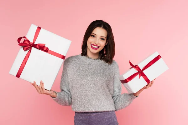 Happy woman in sweater holding presents and looking at camera isolated on pink — Stock Photo
