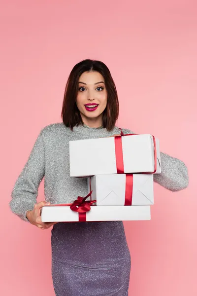 Feliz mujer elegante sosteniendo regalos y mirando a la cámara aislada en rosa - foto de stock