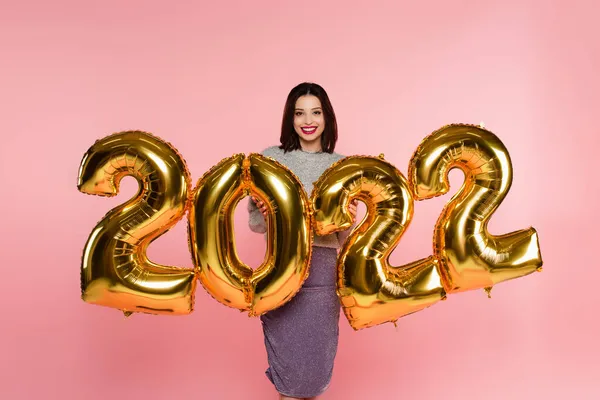 Heureuse femme élégante debout près de ballons en forme de numéros 2022 isolés sur rose — Photo de stock