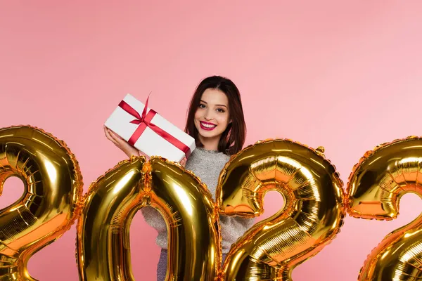 Glückliche Frau hält Geschenk in Form von Luftballons in der Nähe von Zahlen 2022 isoliert auf rosa — Stockfoto