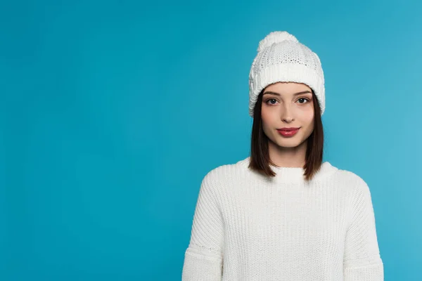 Jolie jeune femme en chapeau blanc et pull regardant la caméra isolée sur bleu — Photo de stock