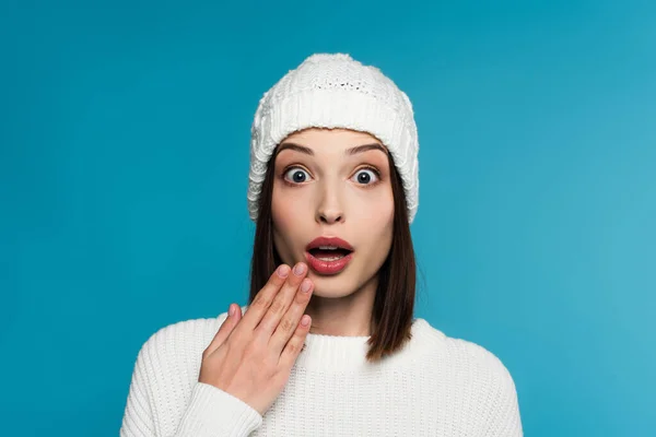 Mujer asombrada en sombrero blanco y suéter mirando a la cámara aislada en azul — Stock Photo